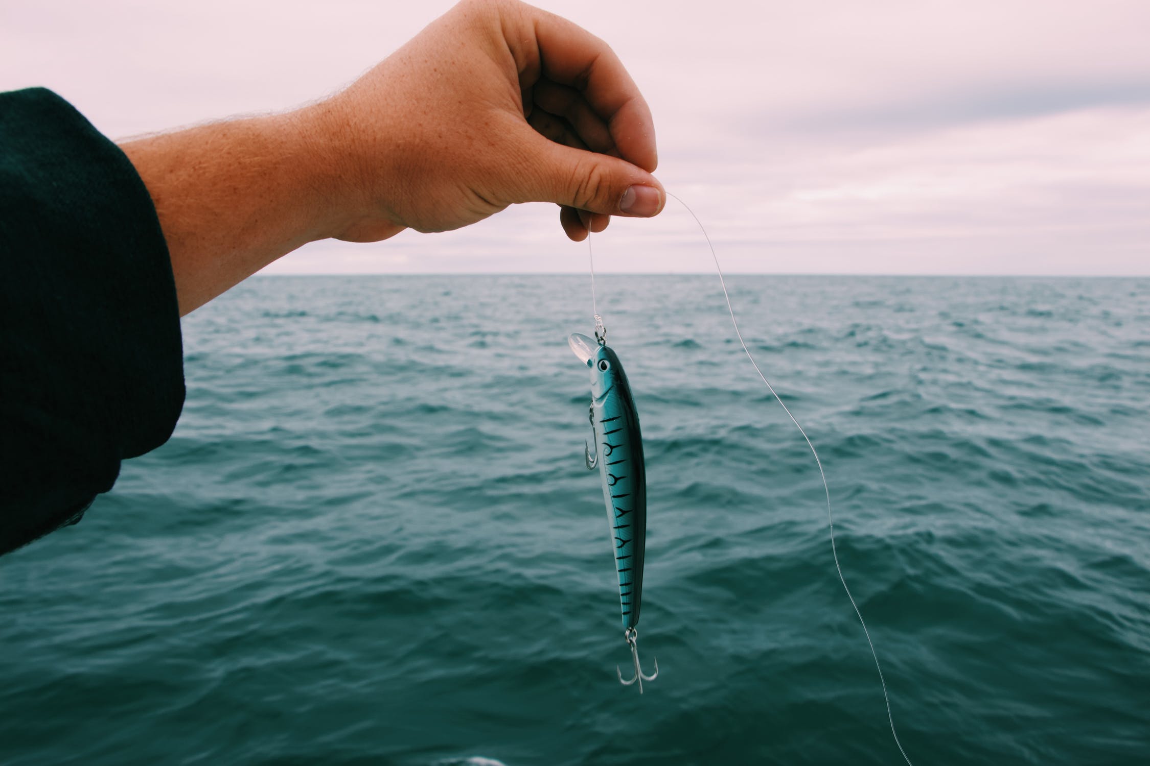 A person holding a striped fishing lure by a fishing line.