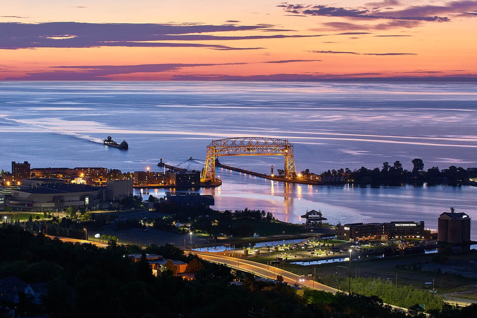An early morning sunrise with a ship coming into Duluth's Aerial Lift Bridge. The bridge's road is raised.