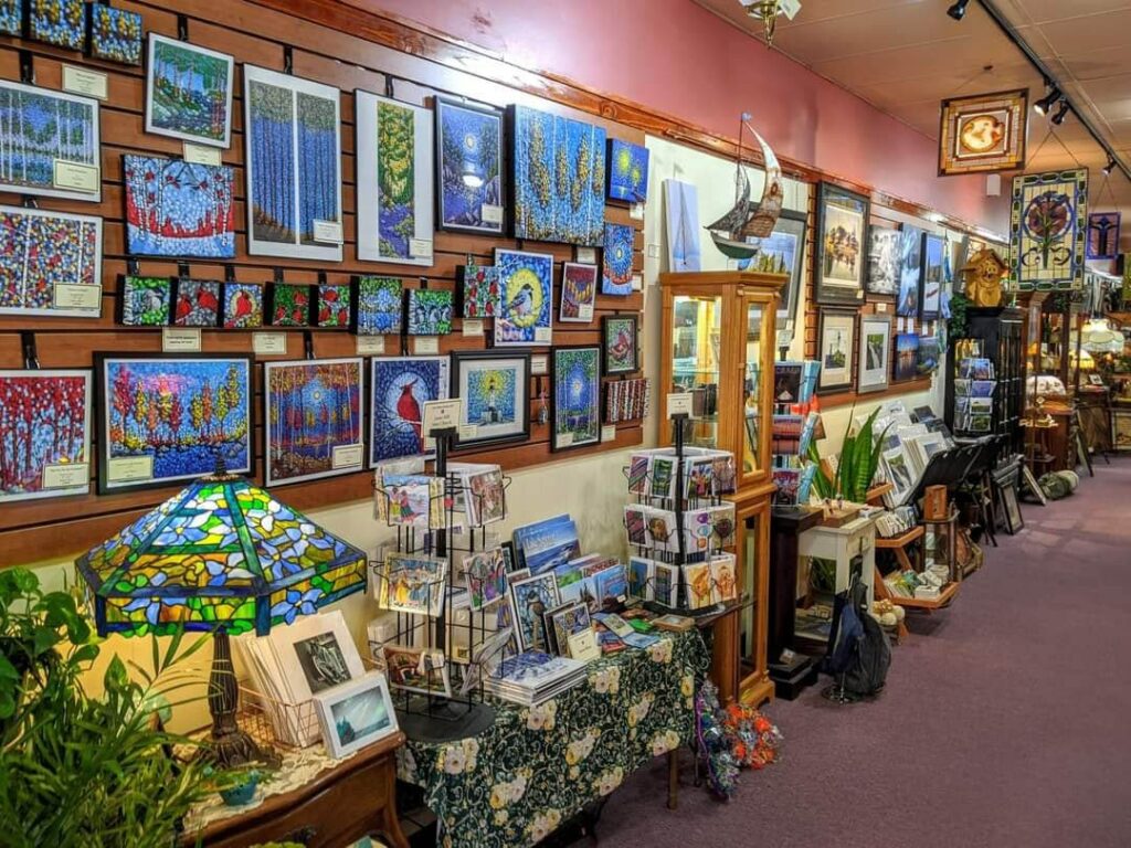 A wall displaying colorful paintings and a stained glass lamp in an art gallery.