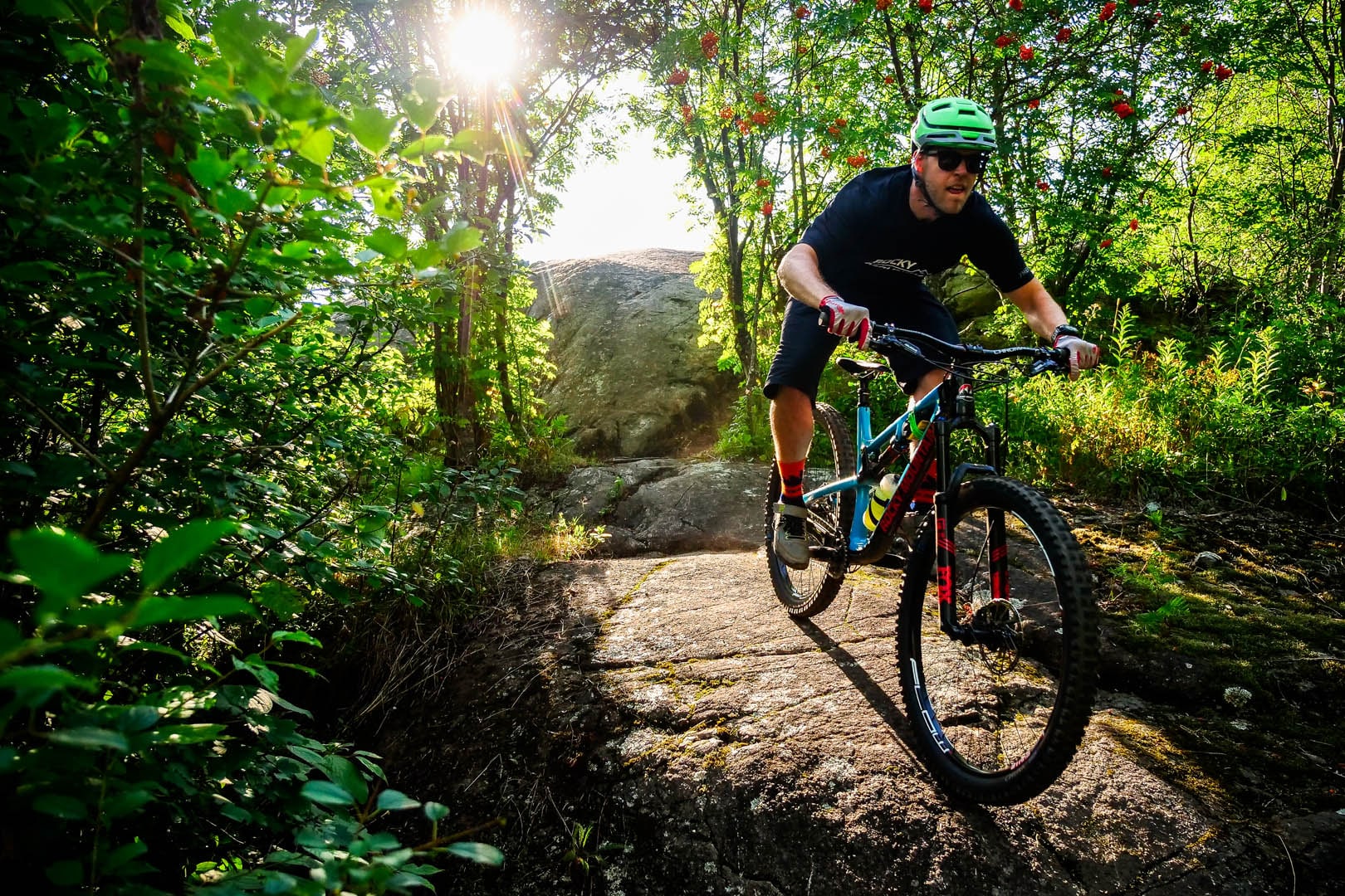 Mountain biker going across volcanic rock. A bright sun shines through the green trees.