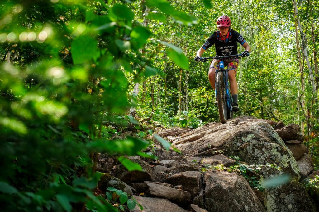 Young mountain biker in a bright green forest riding over volcanic rock in Duluth Minnesota.