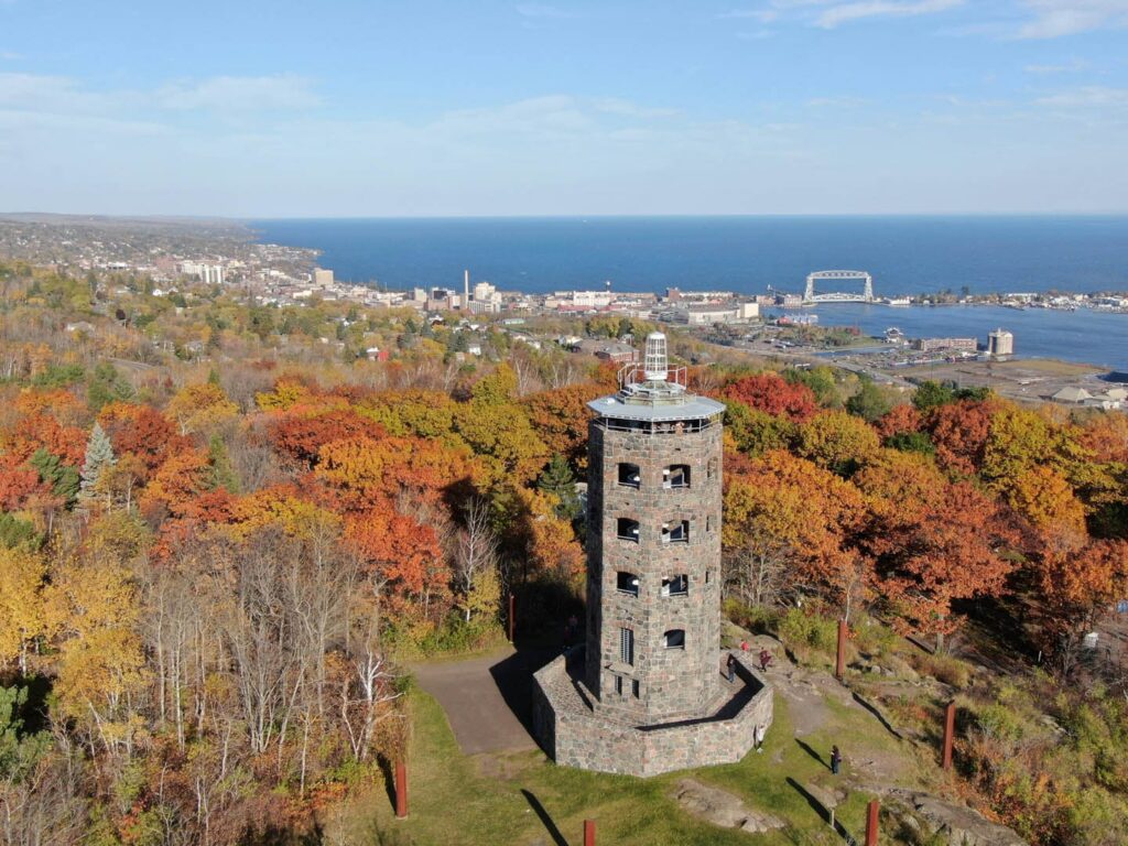 Aerial autumn view of Enger Tower with the blue waters of Lake Superior and the Aerial Lift Bridge in the distance.