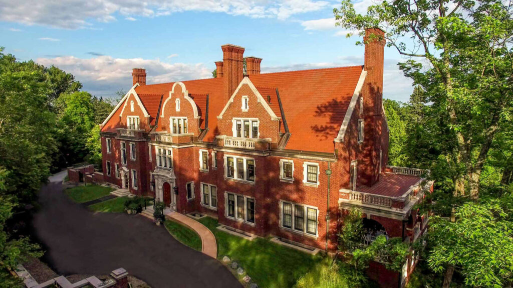 The London Road exterior of the Glensheen Mansion with a warm, sunny glow on it. Trees are green.