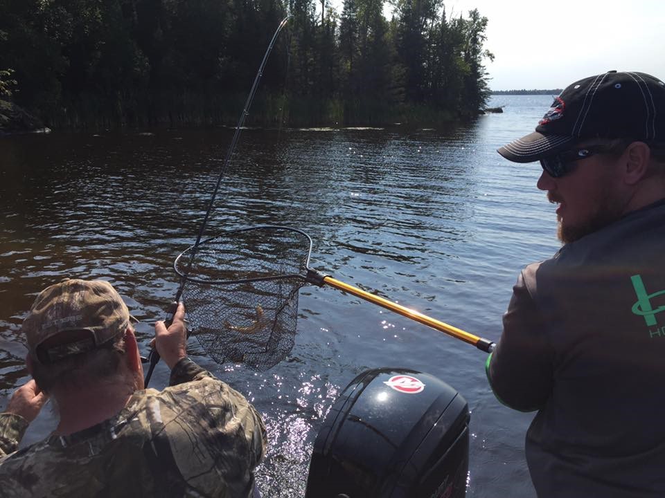 Two men fishing. One holding the net, the other has caught a small northern. This is an inland lake.