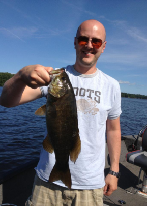 A smiling man holding a bass by the open mouth.