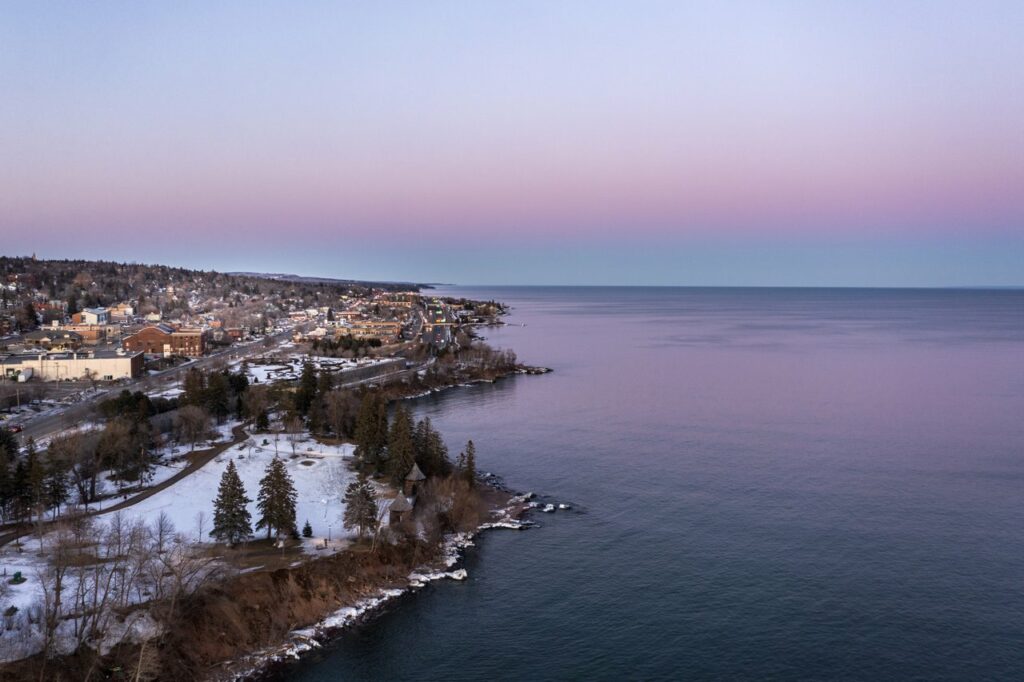 Aerial view of Leif Erikson Park and the shoreline of Lake Superior. The sky and water is pink and purple in color.