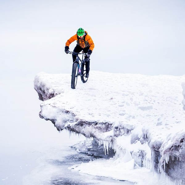 Mountain biker with a bright orange coat, and bright green helmet riding on a rock outing, covered with ice.