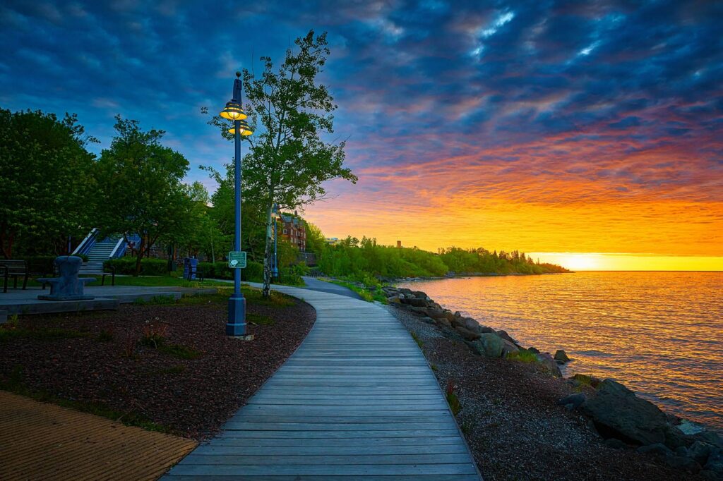 A deep orange, early sunrise along the lakewalk. The clouded sky is dark blue.