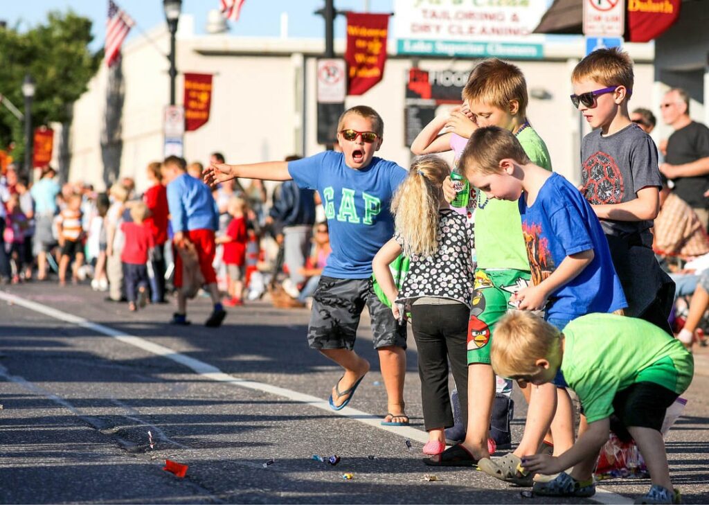 Kids standing along a parade route picking up candy from the road.