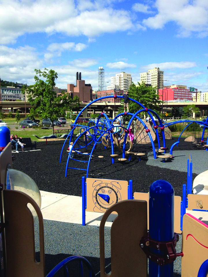 Blue playground equipment for kids at Playfront, with downtown Duluth skyline in the background.