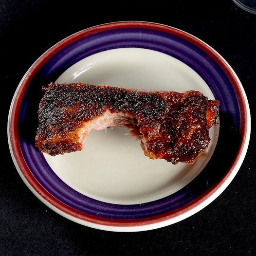 A spare rib with a bite taken out of it on a ceramic plate.