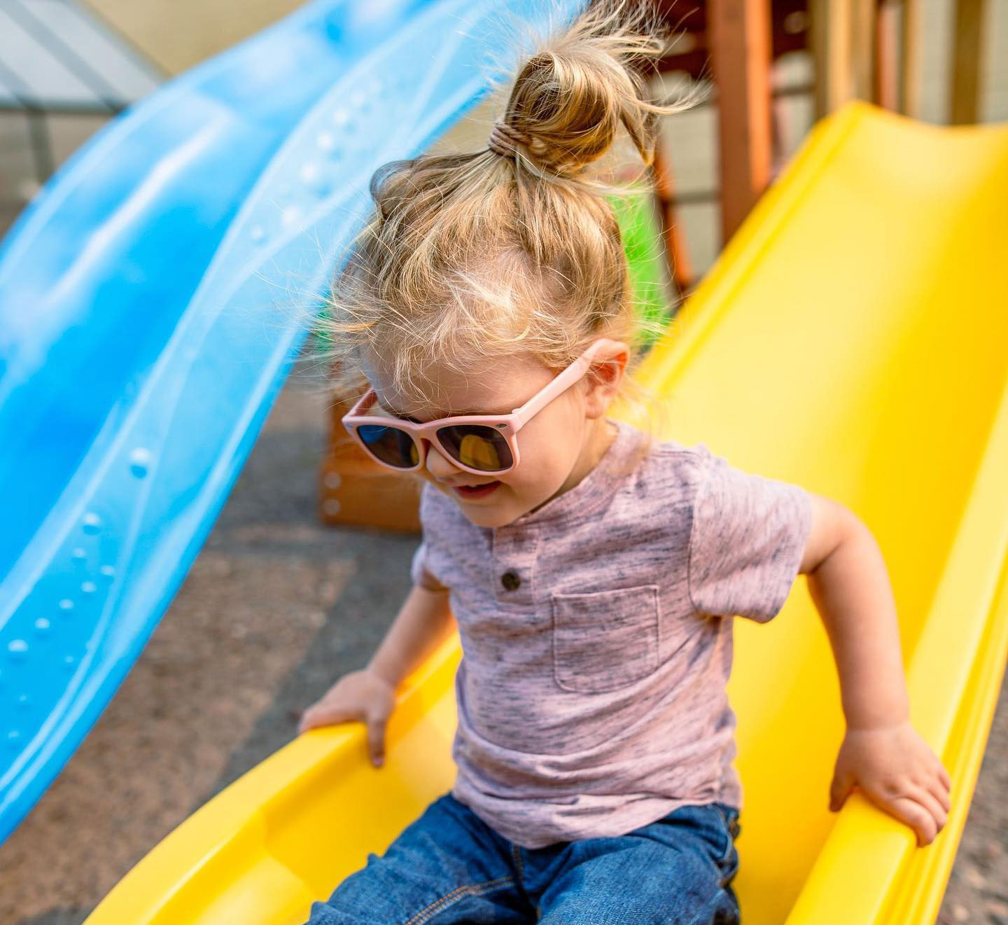 Child going down a yellow slide wearing sunglasses.