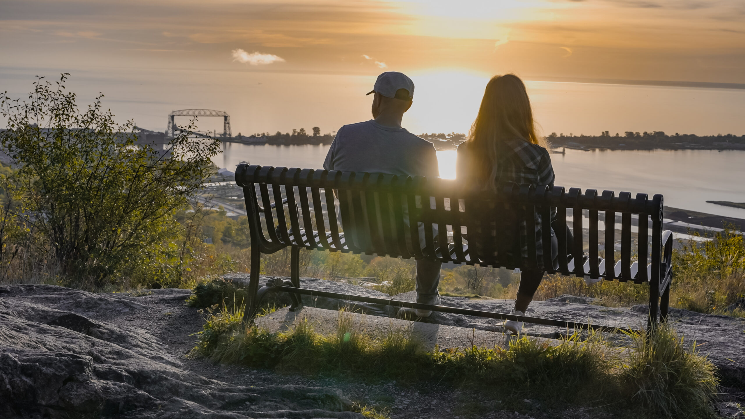 Two people sitting on a bench overlooking Lake Superior at sunset