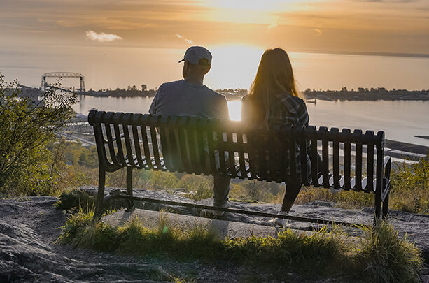 two people sitting on a bench looking out at the lake