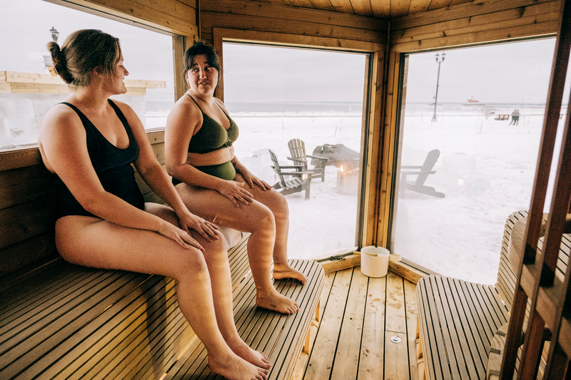 Two people sit in a sauna in winter