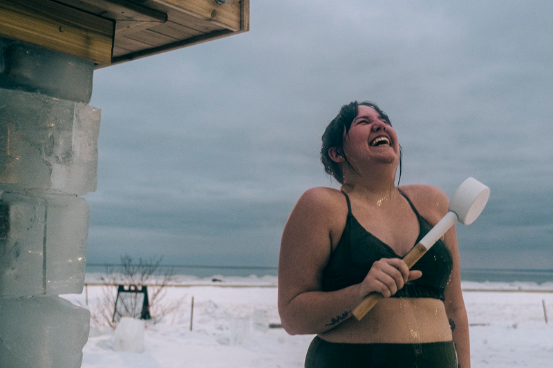 A woman laughs outside of a sauna in winter