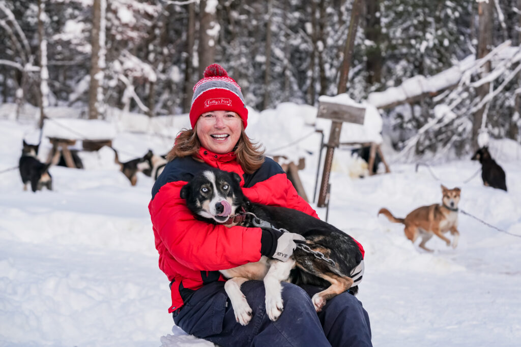 Colleen Wallin smiles while holding one of her dogs as more dogs run in the background