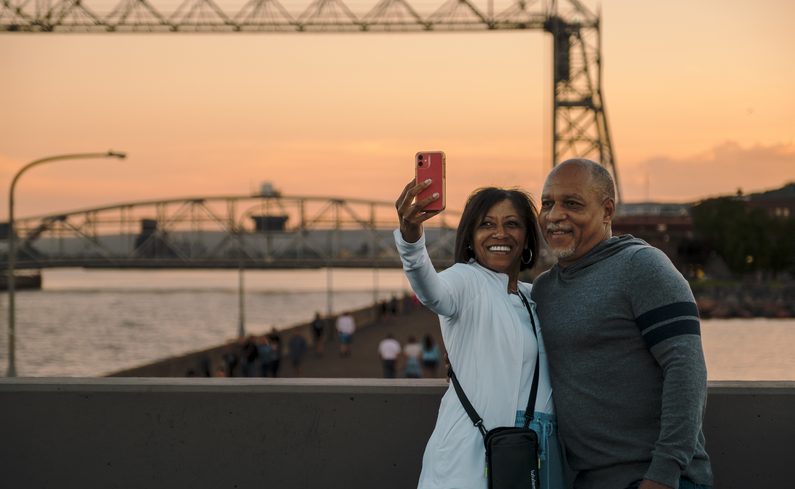 A couple takes a photo in front of the lift bridge at sunset