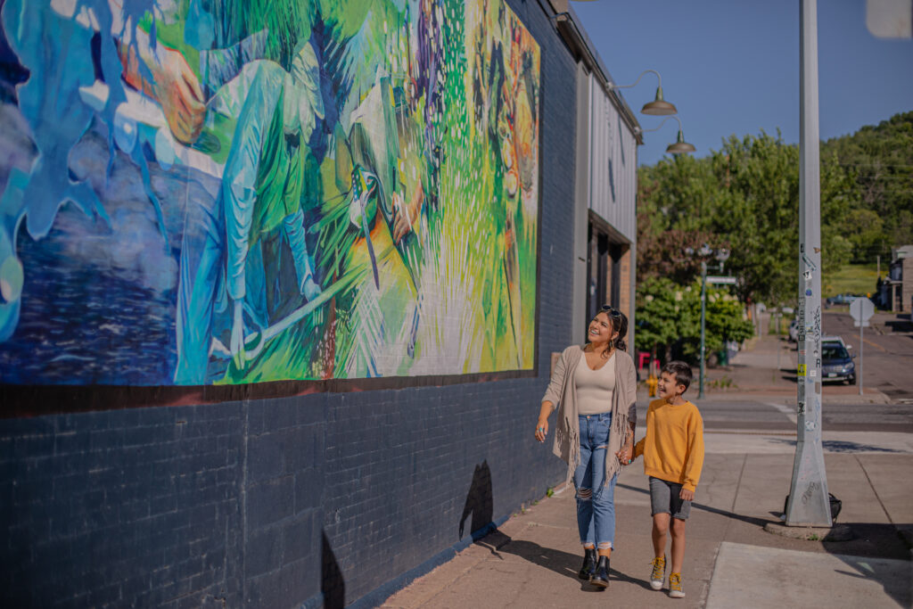 a parent and child walking and admiring a vibrant mural on the outside of a building