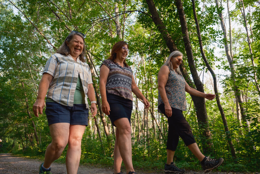 three women hiking on a trail in a lush green wooded area