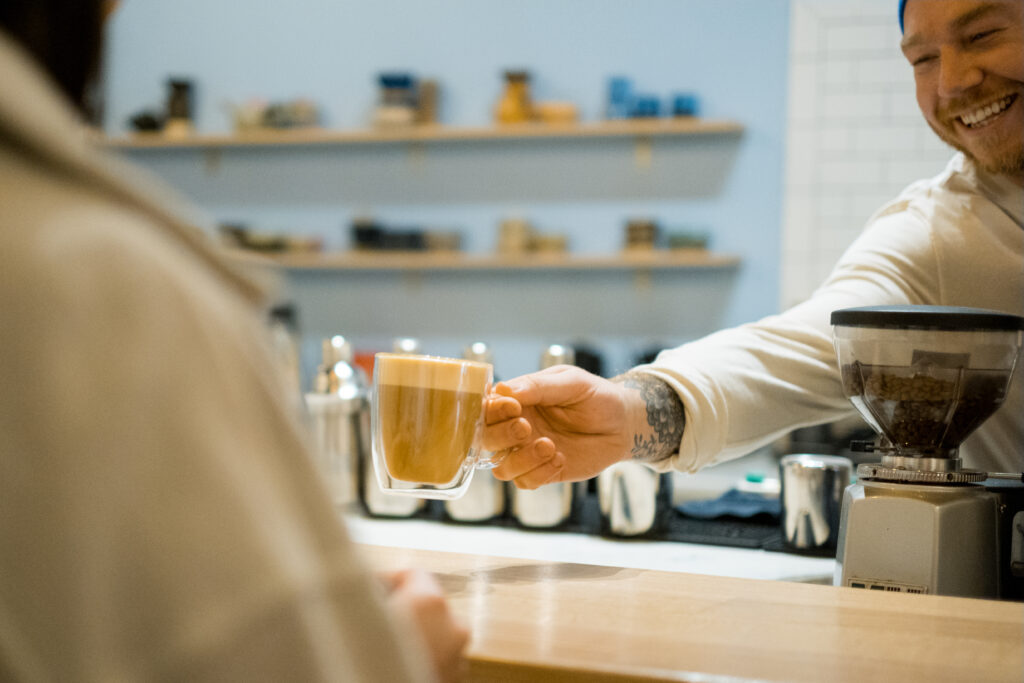 man handing a mug of coffee to customer across a counter at a coffee shop