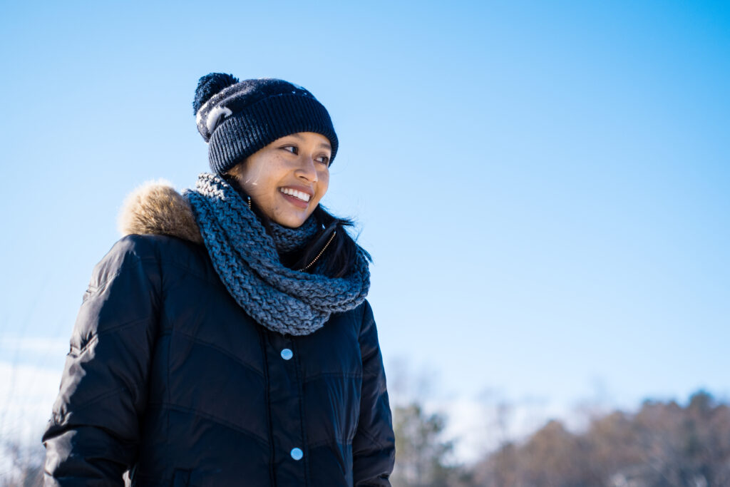 woman in warm hat, scarf and jacket smiling and enjoying a walk outside with a clear blue sky