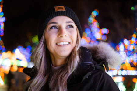 woman in stocking hat smiling with bright holiday lights in the background