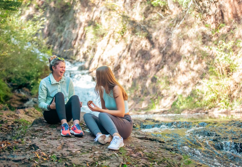 Two women laugh together as they sit on a boulder on the side of the Tischer Creek in Congdon Park of Duluth, Minnesota.