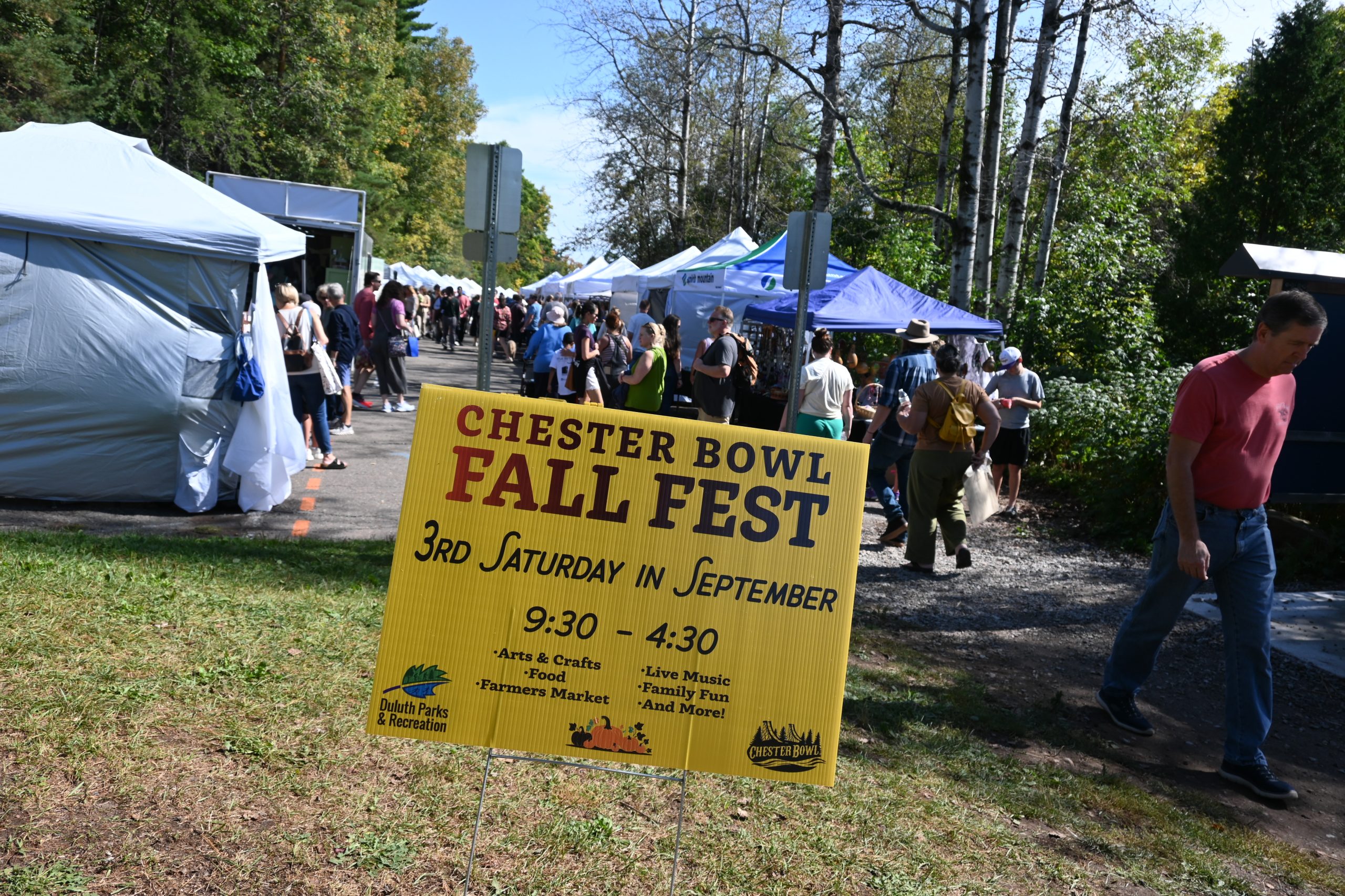 Chester bowl fall fest returns to duluth 2 Chester bowl fall fest yellow event sign on a lawn with crowds of people walking past craft vendor tents in duluth, minnesota.