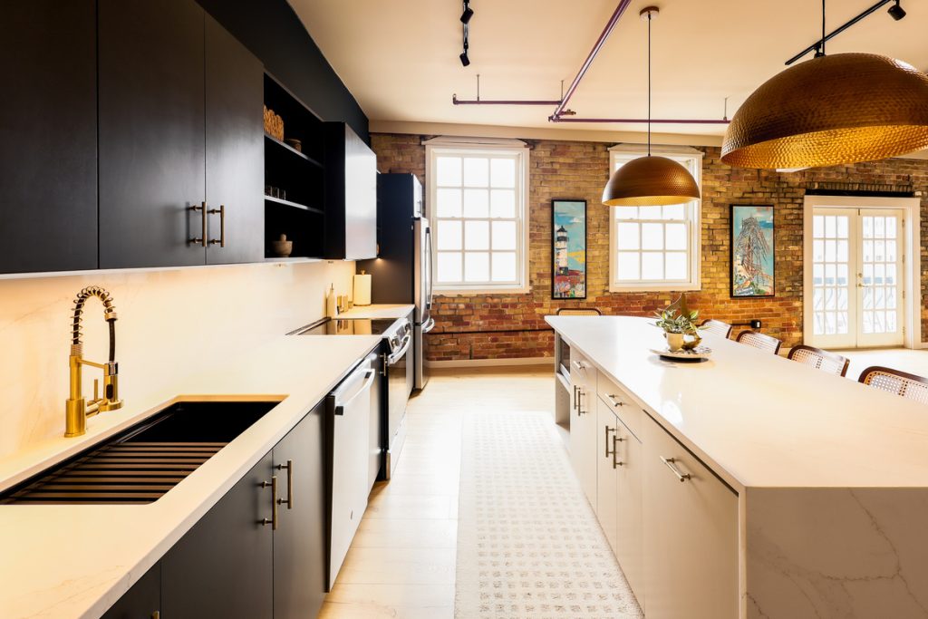 The brix: a different kind of stay in duluth 5 Modern kitchen at the brix aerial lofts in canal park, featuring dark cabinetry, white quartz countertops, exposed brick walls, and local duluth artwork.