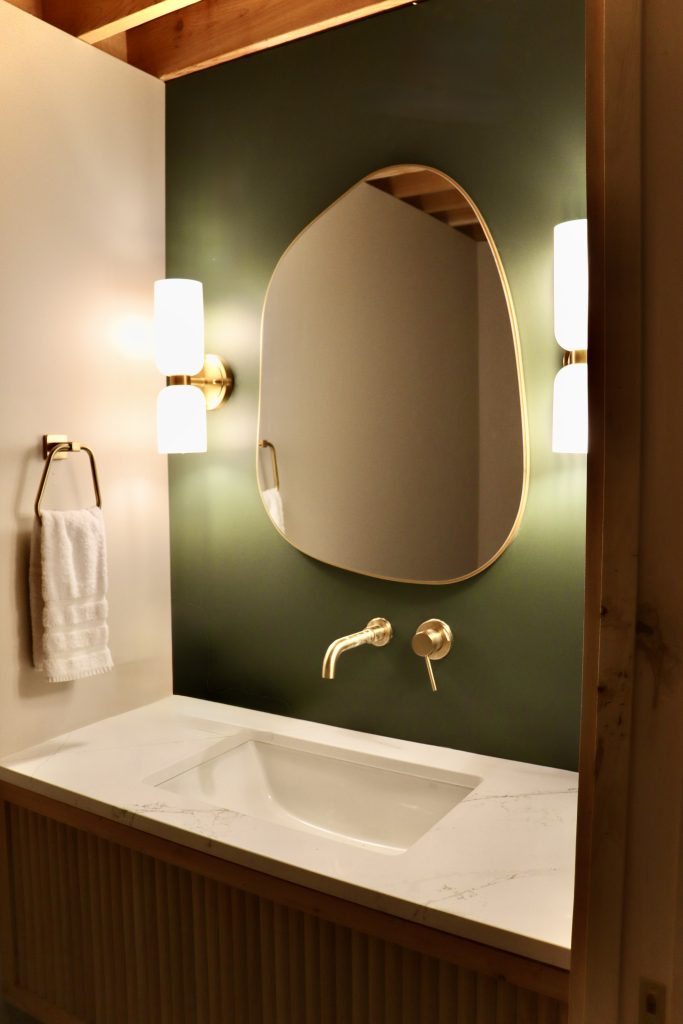 The brix: a different kind of stay in duluth 10 Bathroom vanity at the brix aerial lofts in canal park, featuring an organic modern mirror, brass wall faucet, warm sconces, and deep green walls.