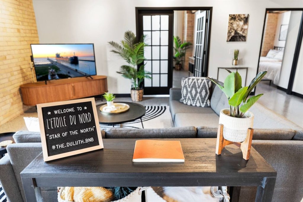 The brix: a different kind of stay in duluth 7 Modern living room at the brix l'etoile du nord vacation rental in duluth, featuring exposed brick, comfortable seating, and a welcome letterboard sign.