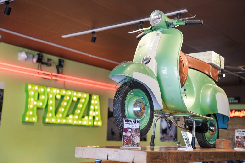 How vitta pizza became a duluth favorite 9 A vintage green vespa display scooter inside the vitta pizza dining room with a lit marquee sign spelling out pizza on the wall.