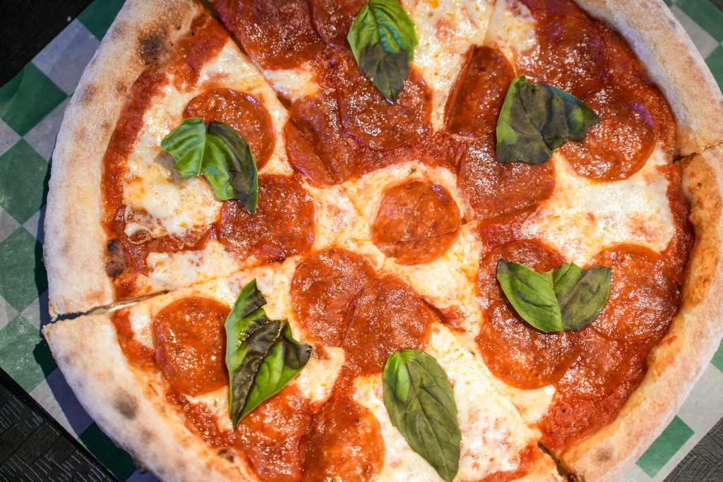 How vitta pizza became a duluth favorite 8 Overhead view of a sliced wood-fired pepperoni pizza topped with melted mozzarella and fresh basil leaves at vitta pizza in duluth.