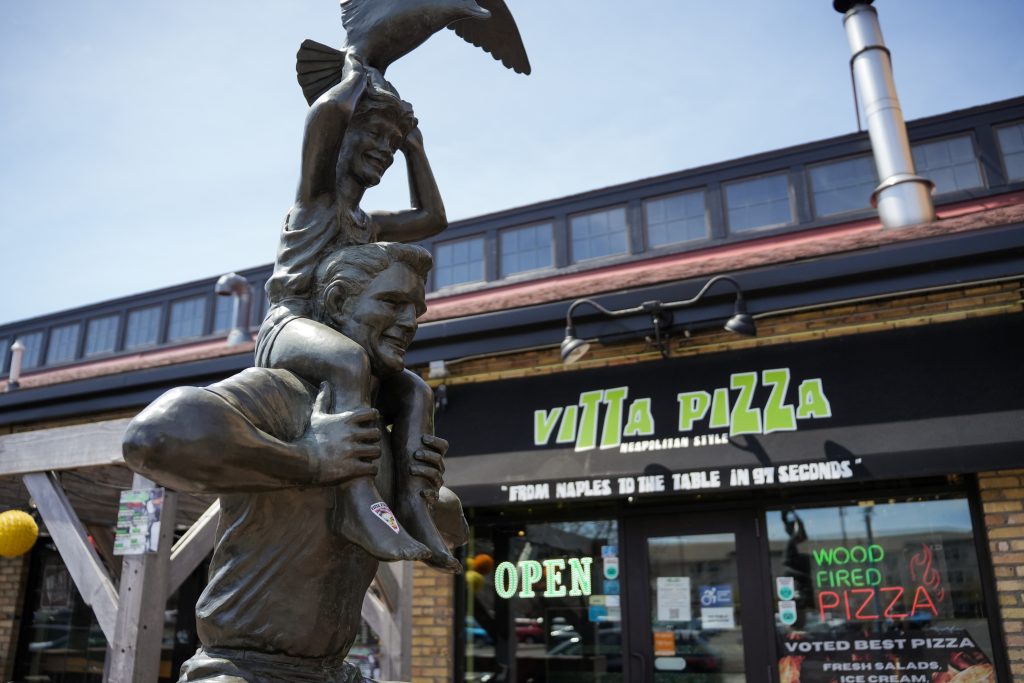 How vitta pizza became a duluth favorite 10 Exterior view of vitta pizza in canal park featuring a bronze statue of a child on a man's shoulders holding a bird in front of the storefront entrance.